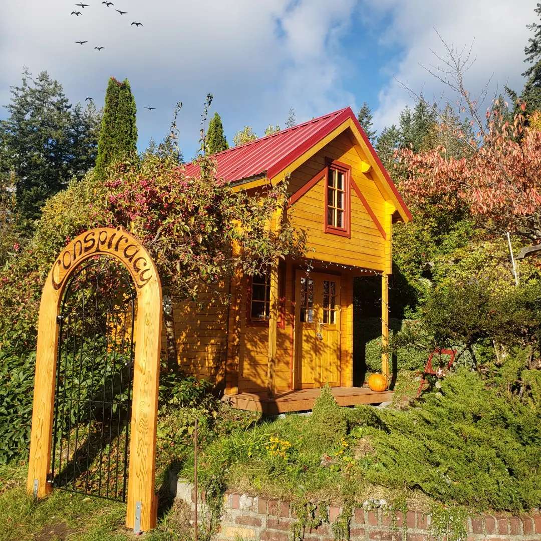 A small hut with a red roof. The wooden archway at the beginning of the path says "Conspiracy" along the top.